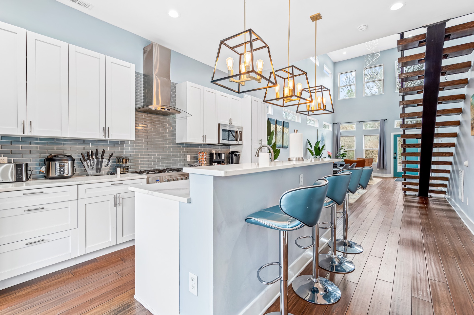 Kitchen island with quartz counter and teal bar stools under pendant lights