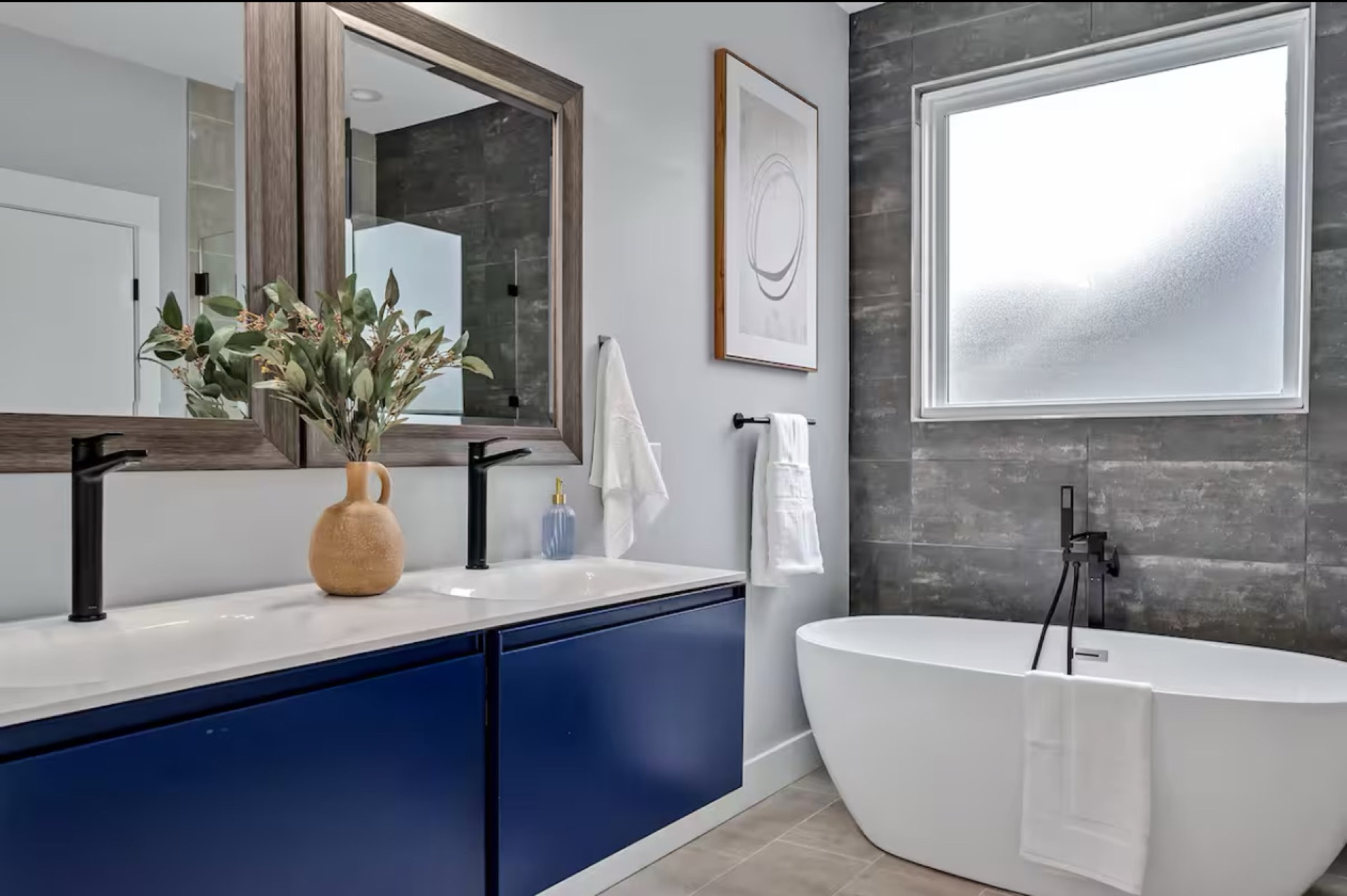 Modern master bathroom with navy vanity, white quartz countertop, freestanding soaking tub, and dark textured accent wall