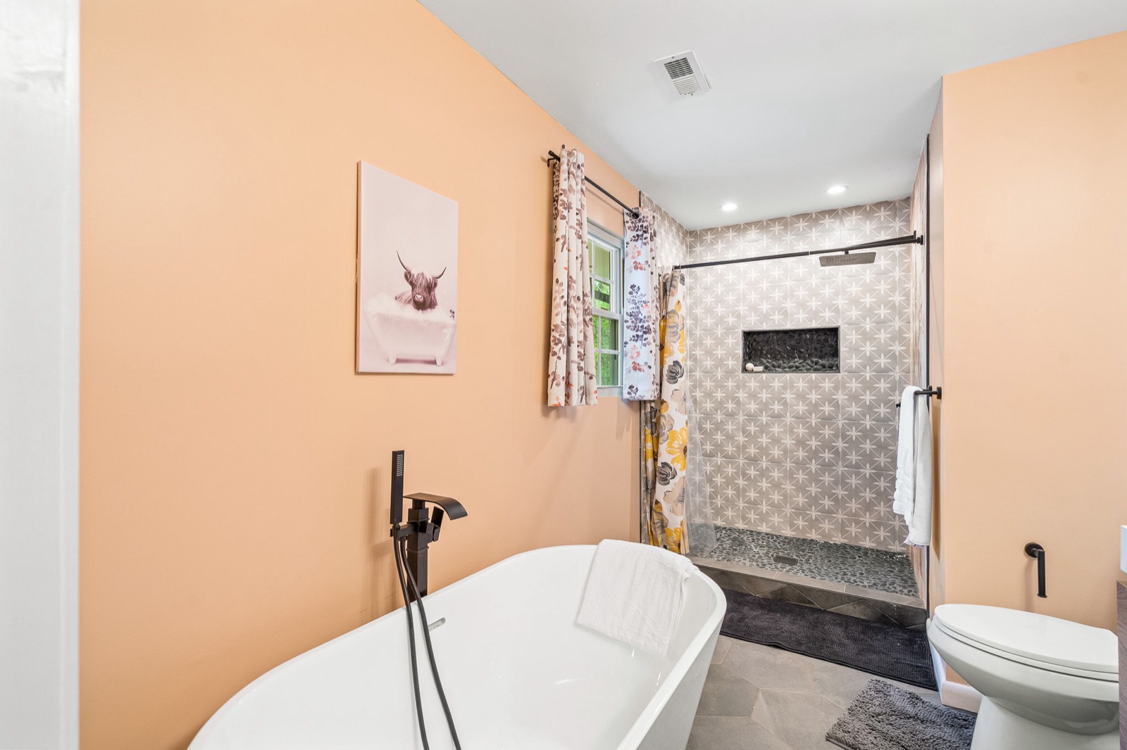 Renovated bathroom with freestanding soaking tub, matte-black fixtures, and a glass walk-in shower with patterned star tile
