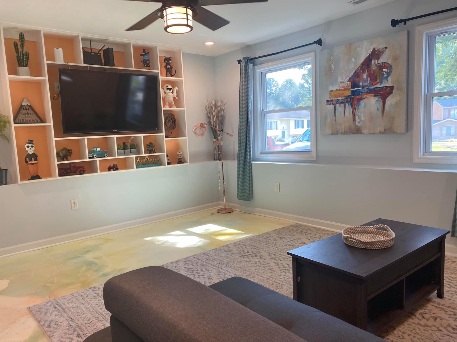Bright family room with floor-to-ceiling white built-in shelving, wall-mounted television, and ceiling fan