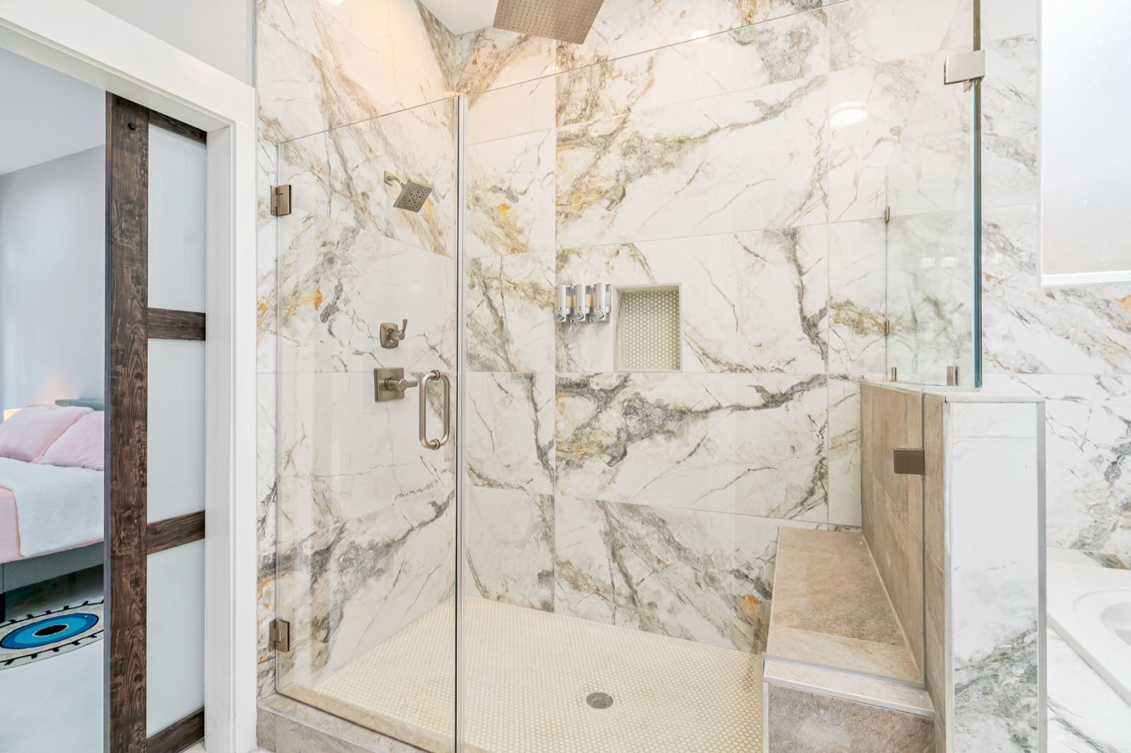 Frameless glass walk-in shower with veined marble-look slab walls, built-in bench, and brushed-nickel fixtures