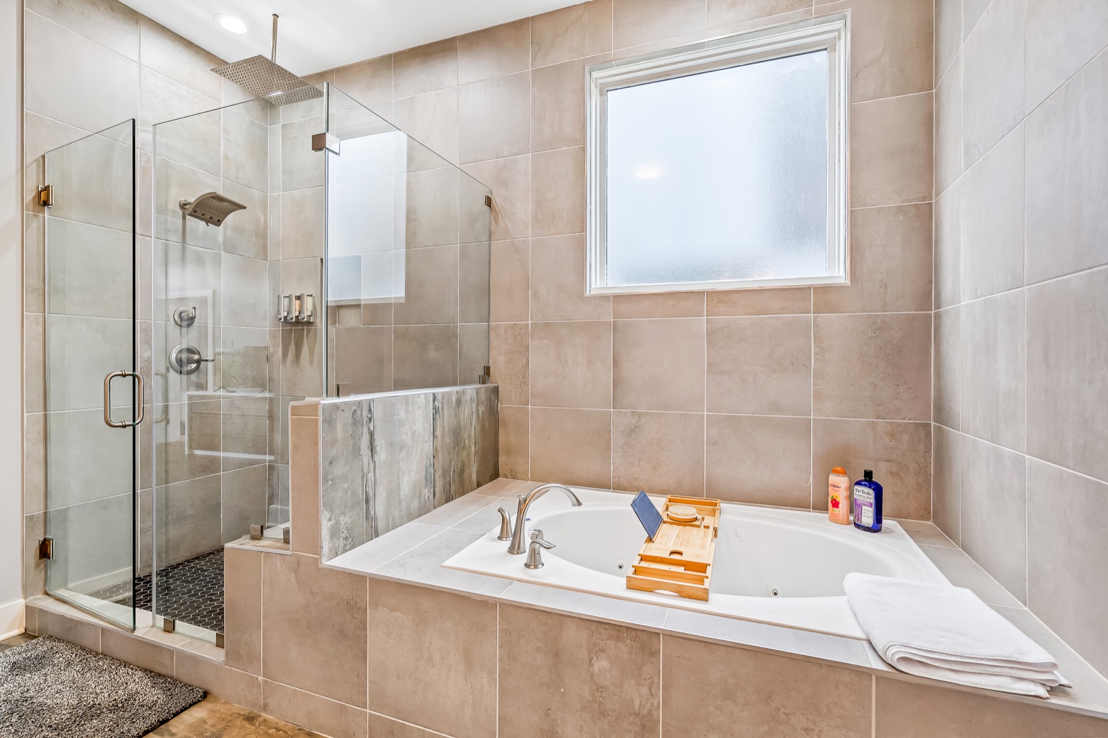 Master bathroom with a frameless glass walk-in shower and rainfall showerhead beside a tiled soaking tub under a frosted privacy window
