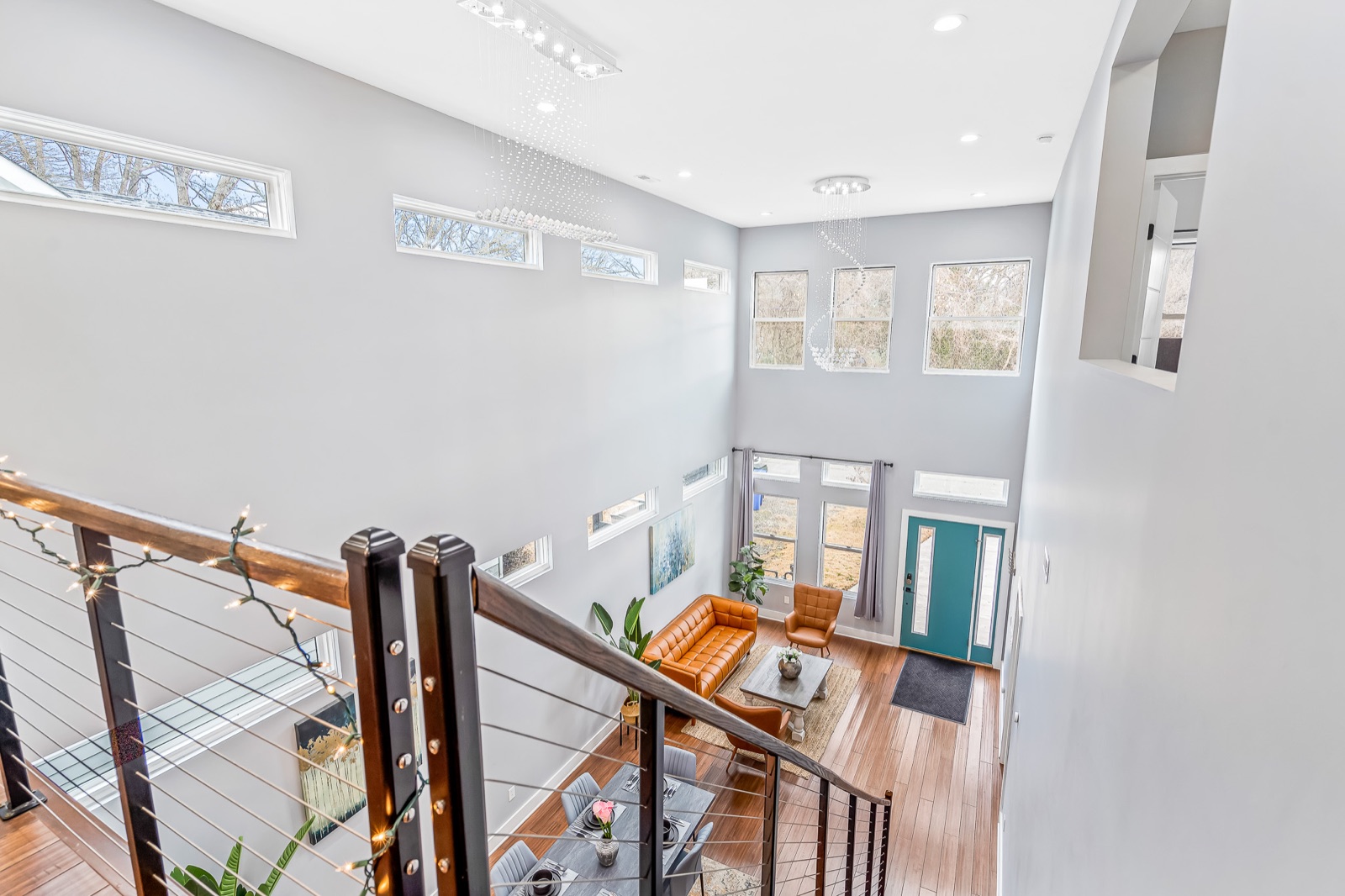Two-story foyer and living room seen from an upper landing, featuring a teal front door, leather sofa, accent chair, and tall windows